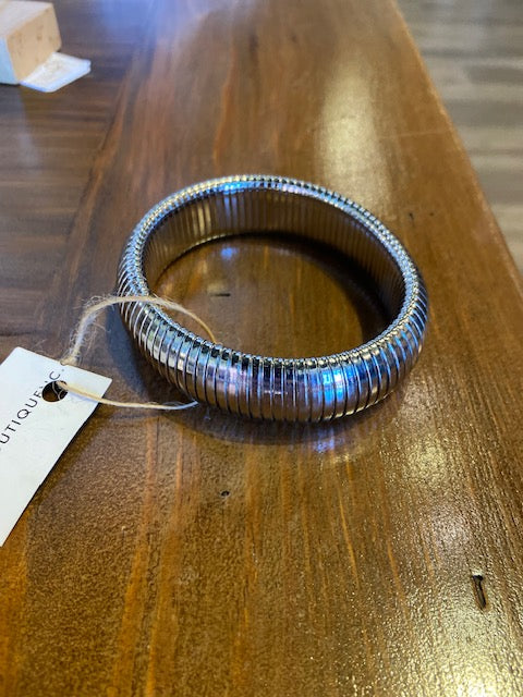 Metallic bracelet on a wooden surface with a visible brand tag.