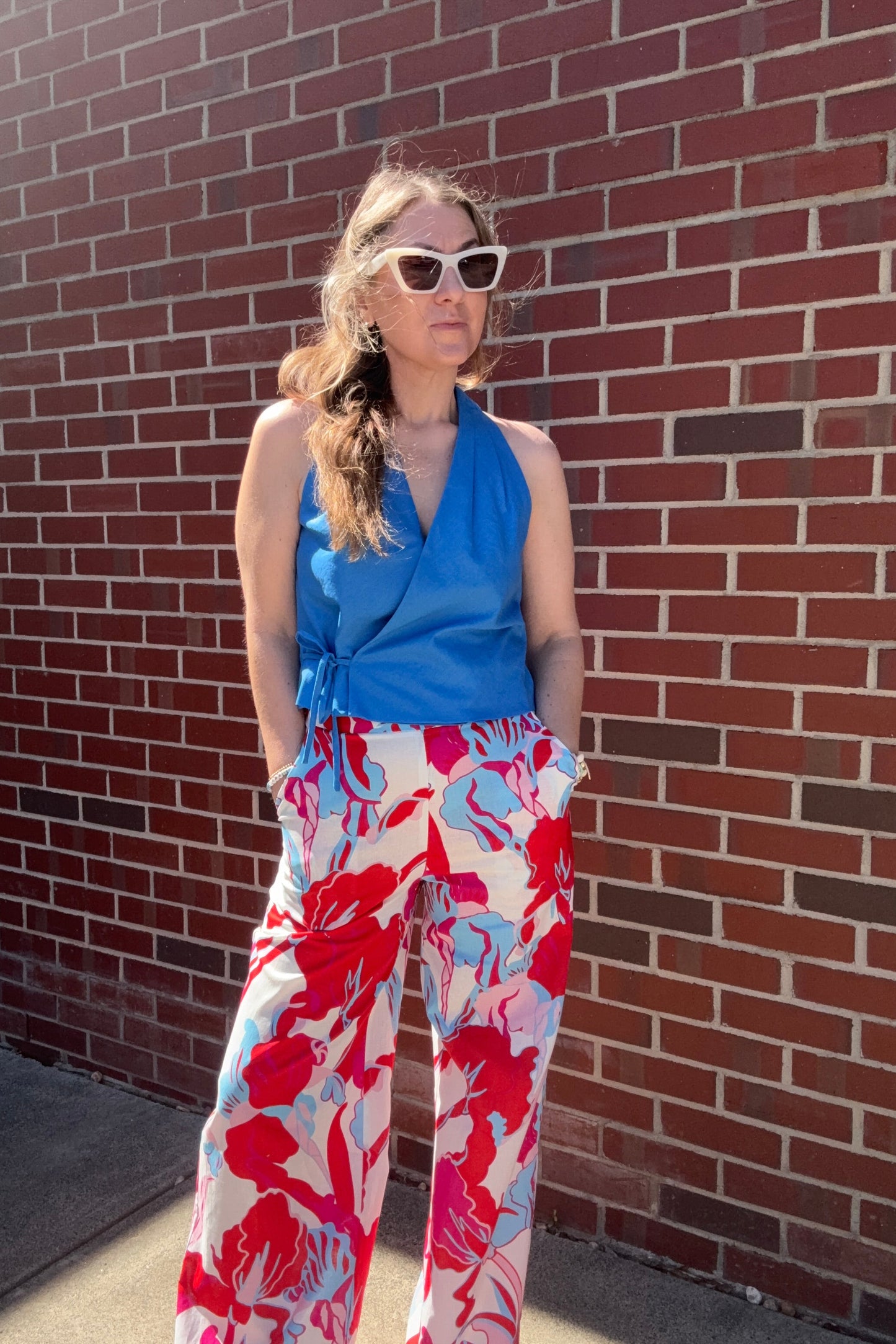Person wearing a blue top and red floral pants on a brick pavement