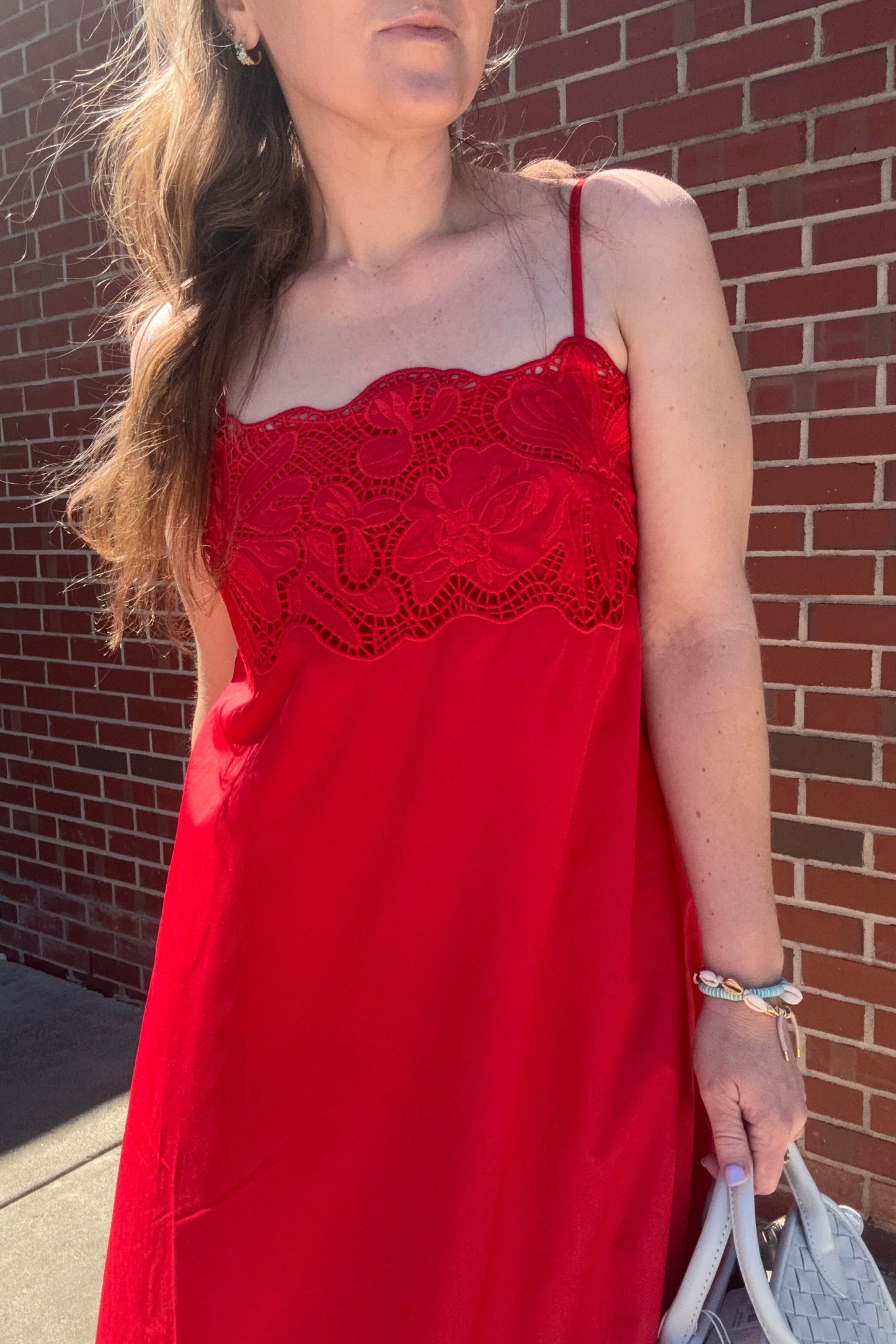 Person wearing a red dress with lace details on a brick pavement