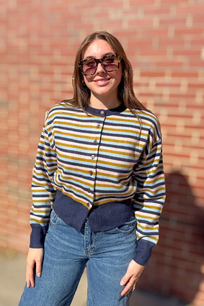 Woman wearing a striped shirt and sunglasses standing against a brick wall.