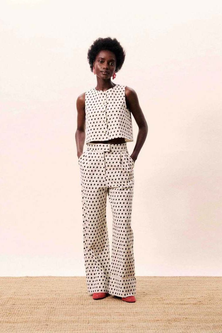 Person wearing a polka dot sleeveless top and wide-leg pants on a plain background