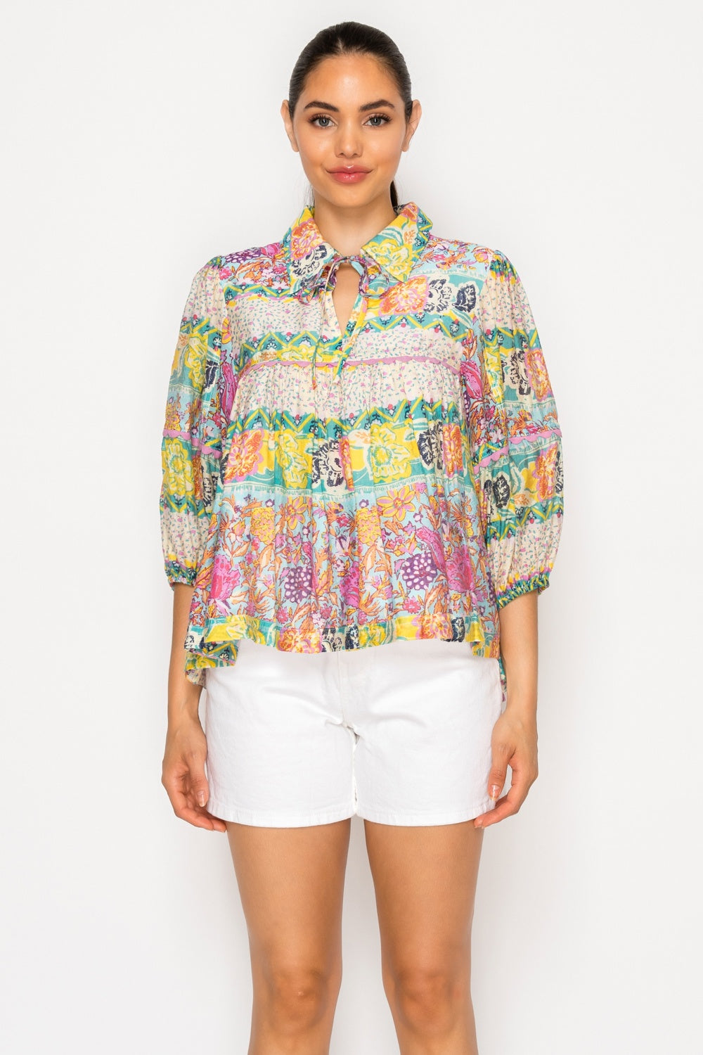 Woman wearing a colorful patterned blouse and white shorts on a white background