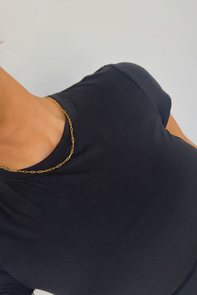 Person wearing a navy blue top with a gold chain necklace on a light gray background