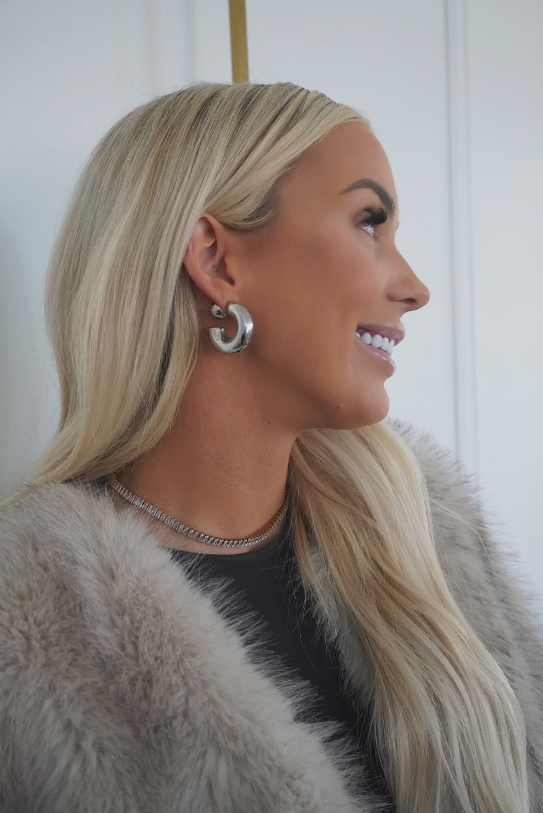 Woman with blonde hair wearing earrings and a fur coat against a white background
