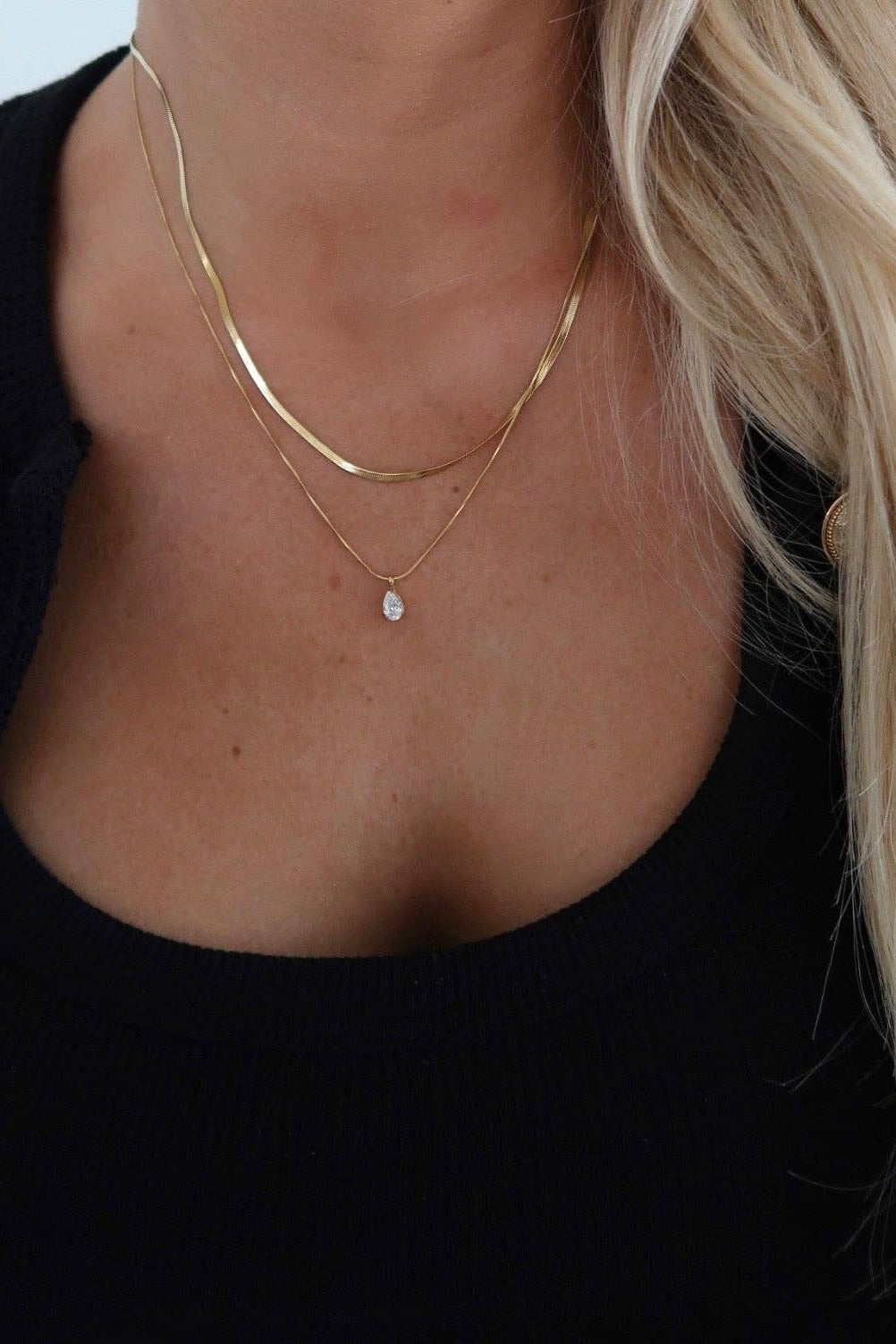 Close-up of a person wearing two gold necklaces with a black background