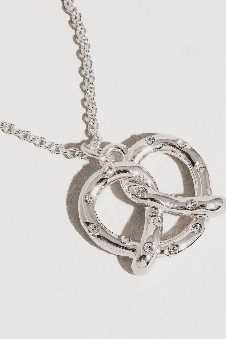Silver necklace with a heart-shaped pendant on a light gray background
