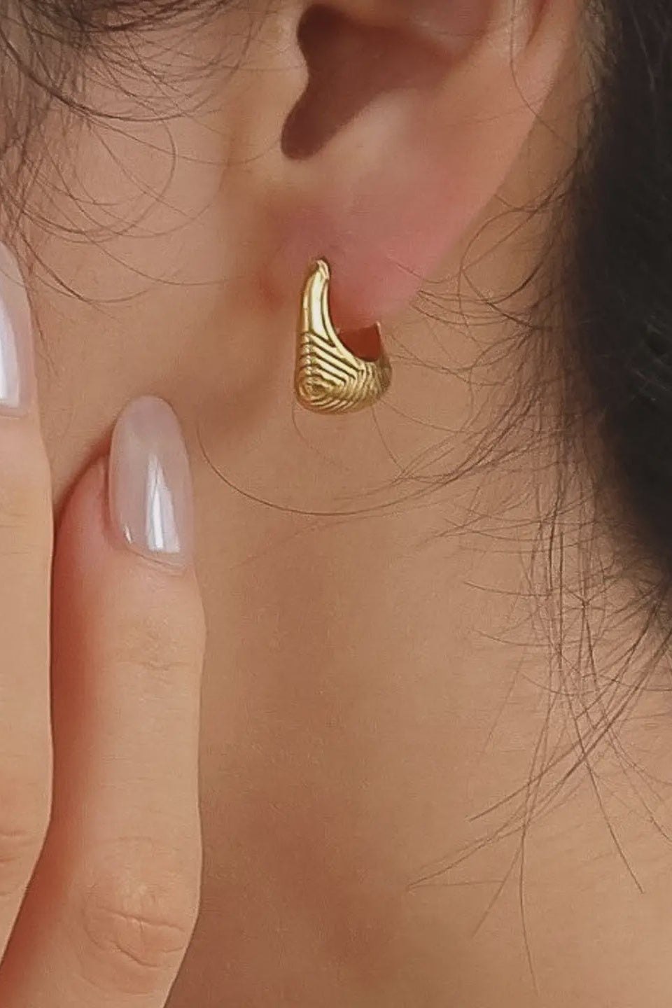 Gold earring worn by a person with a close-up of the ear and hand.