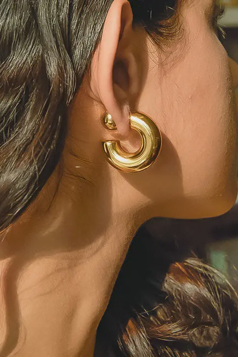 Close-up of a person wearing a gold hoop earring with a blurred background