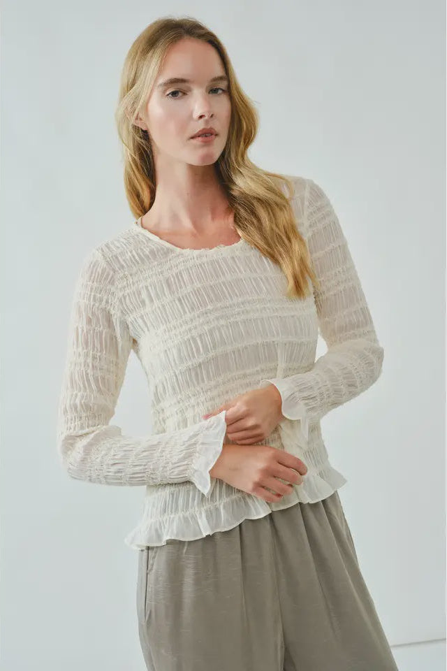 Woman wearing a white textured top and beige pants against a light gray background