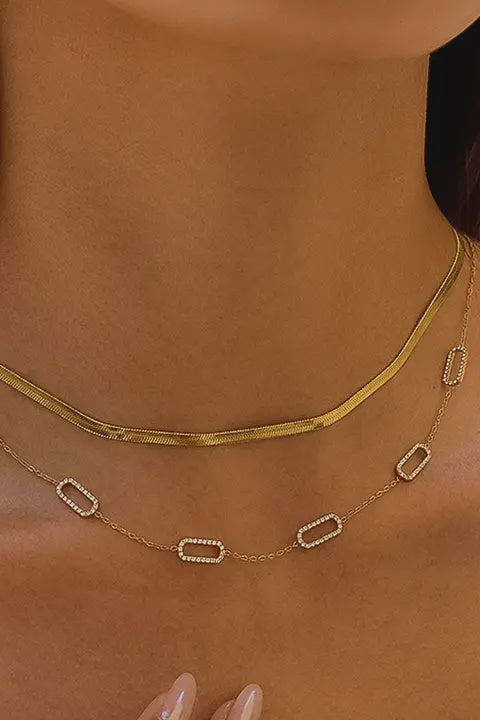 Gold necklace with rectangular pendants on a person's neck against a neutral background
