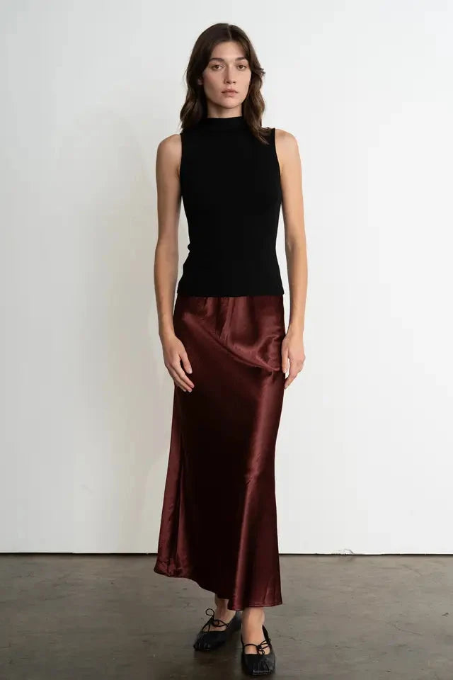Woman wearing a black sleeveless top and burgundy satin skirt against a white background