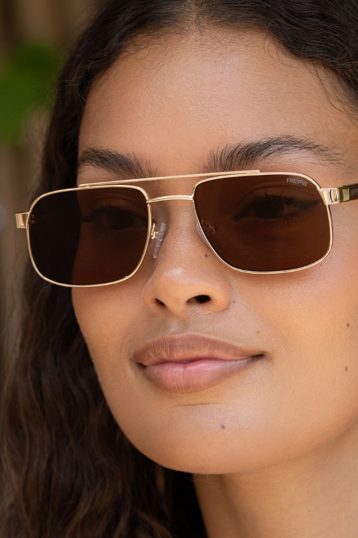 Close-up of a person wearing gold sunglasses and earrings with a blurred natural background