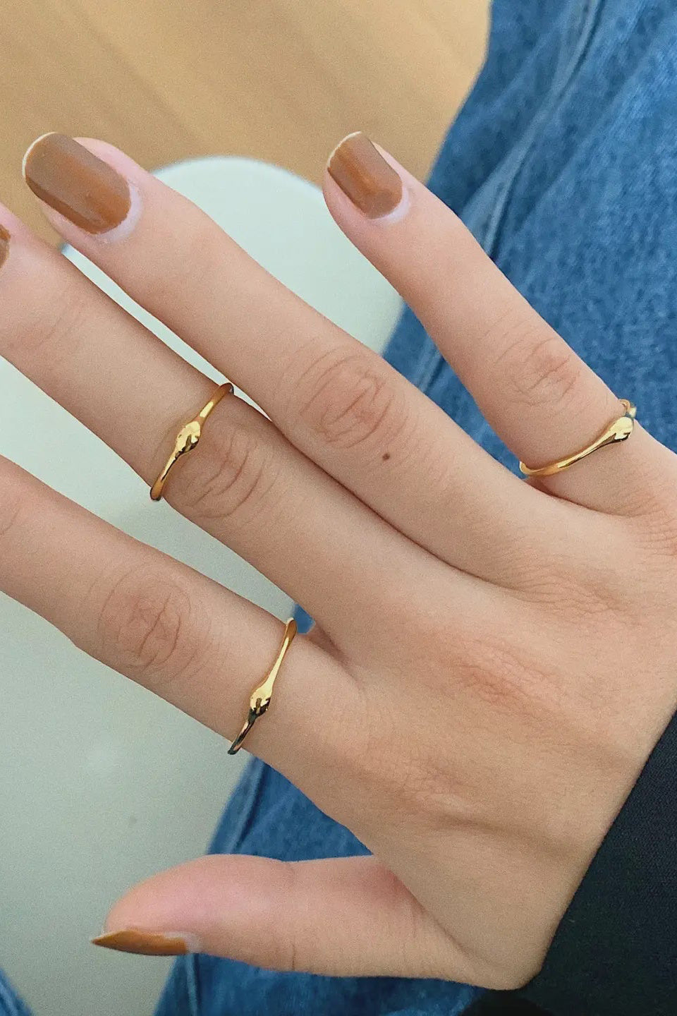Hand with brown nail polish wearing three gold rings on a blurred background