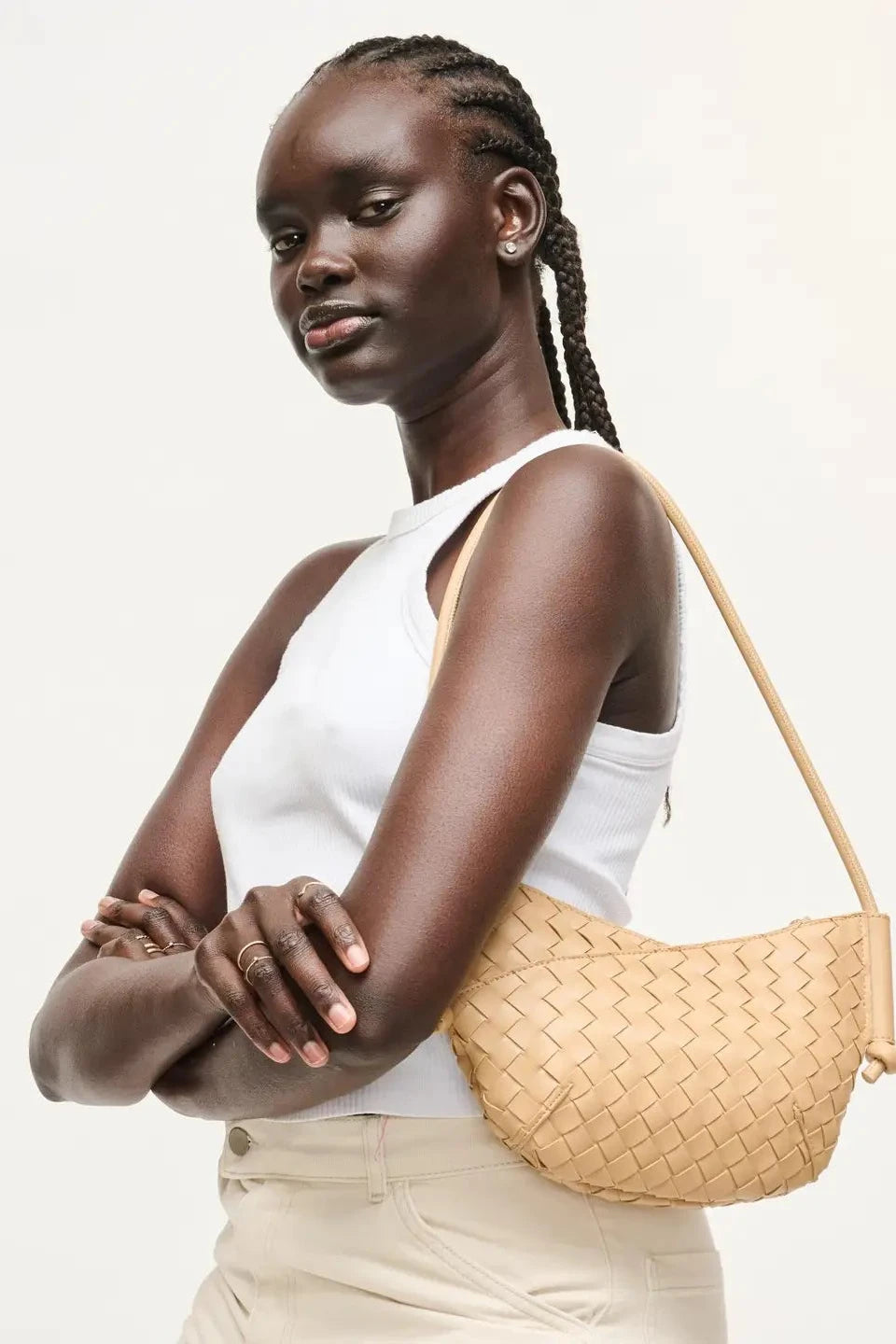 Woman holding a woven beige handbag against a plain background