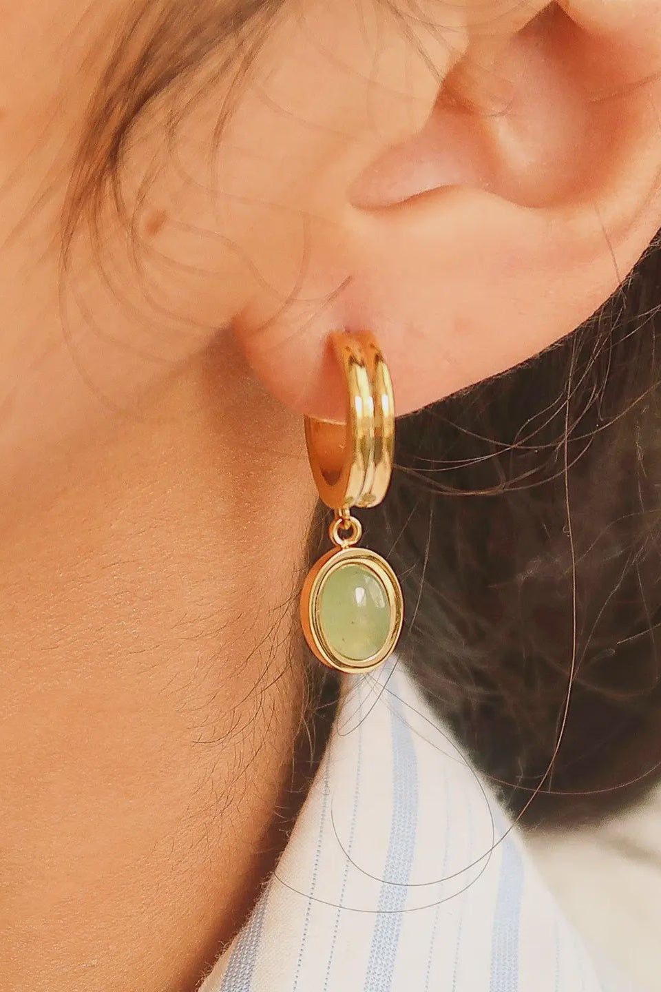 Gold hoop earring with a green gemstone worn by a person.