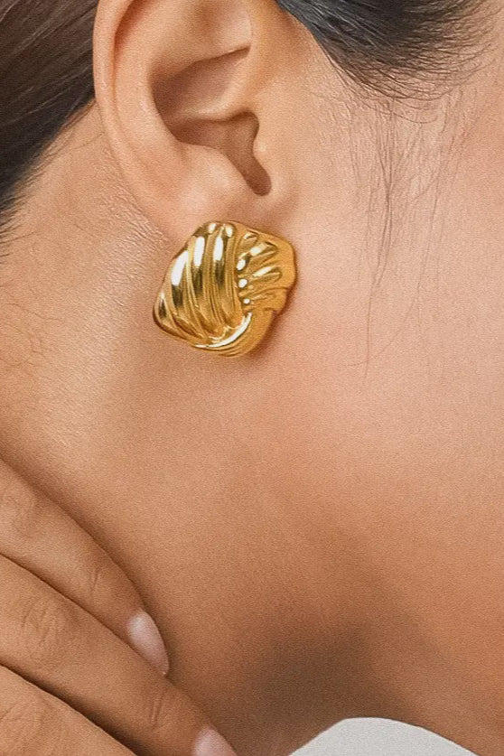 A close-up image of a person's ear wearing a gold-colored wavy square stud earring.