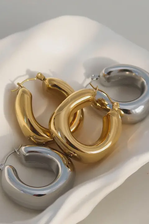 A pair of 18-karat gold non-tarnish classic U-hoop earrings placed on a white dish with a soft white background.