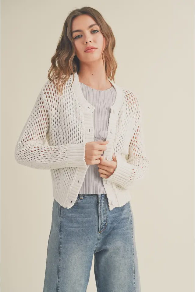 Woman wearing a light-colored knit cardigan over a striped shirt with jeans on a plain background