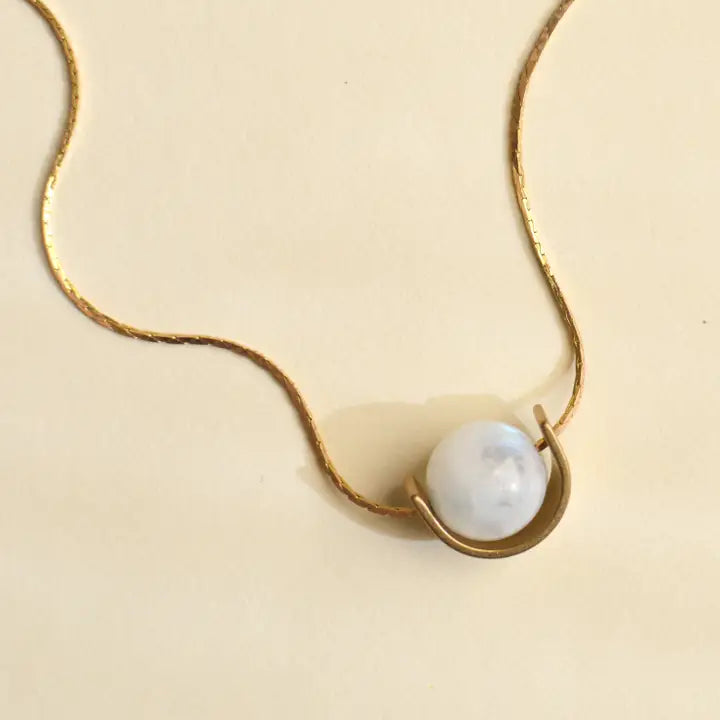 Gold necklace with a pearl pendant on a beige background