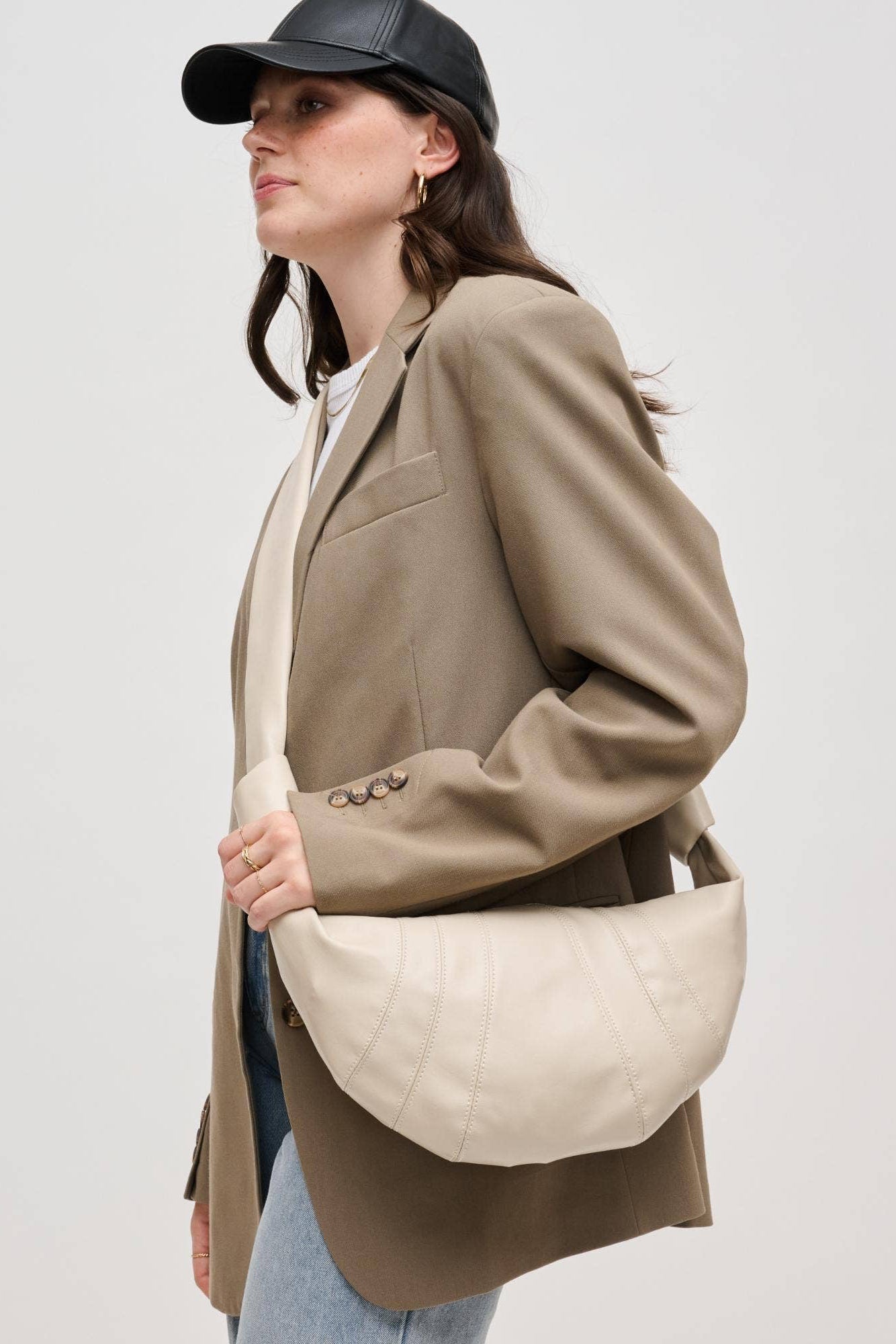 Woman wearing a beige blazer and holding a quilted beige handbag against a plain background