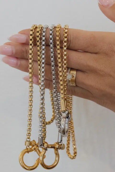 Hand holding three gold chains against a neutral background