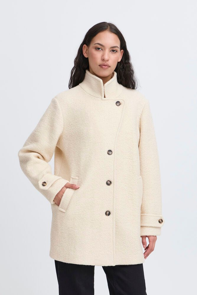 Woman wearing a cream-colored coat with button details on a white background