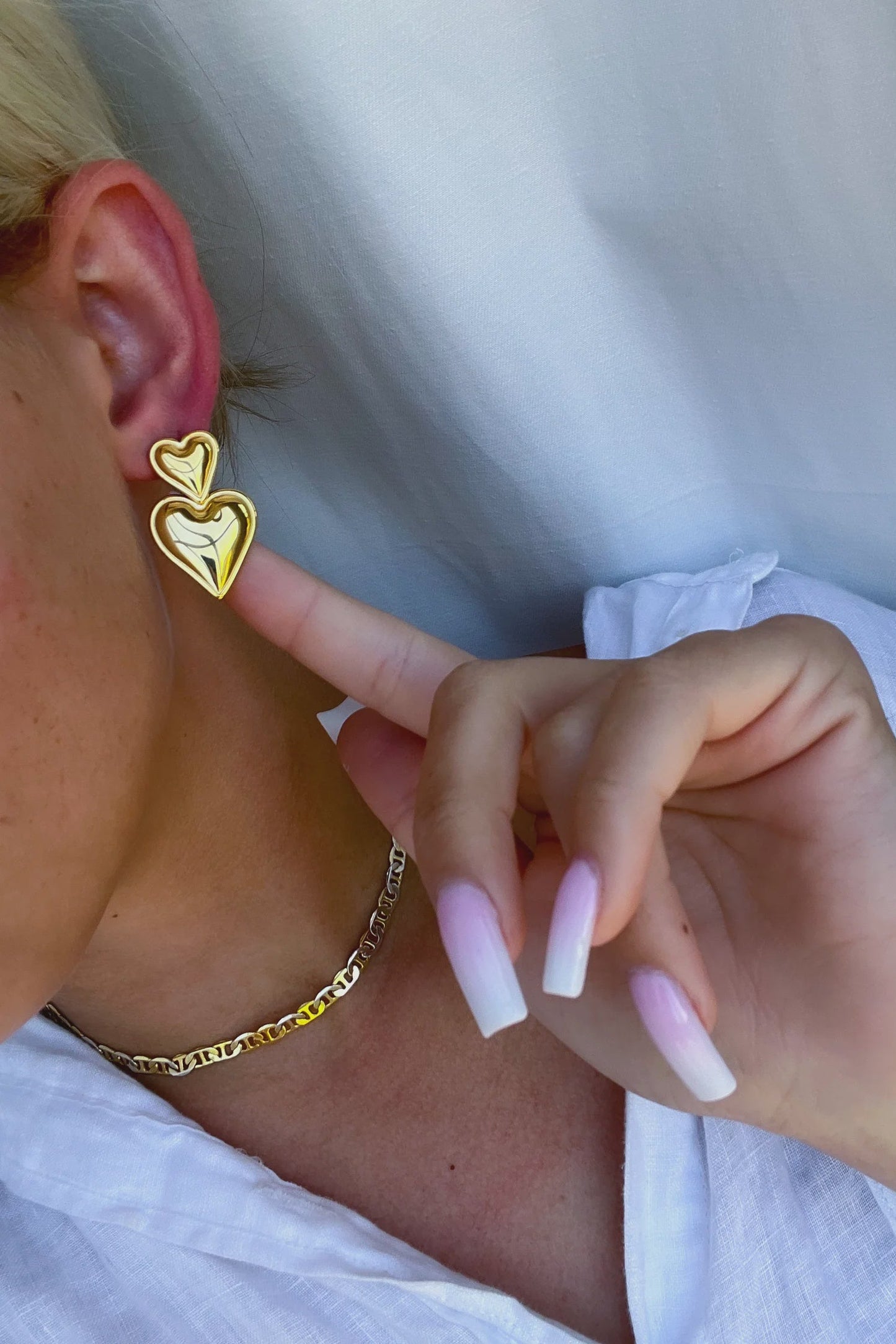 Gold heart-shaped earrings worn by a person with pink nail polish.