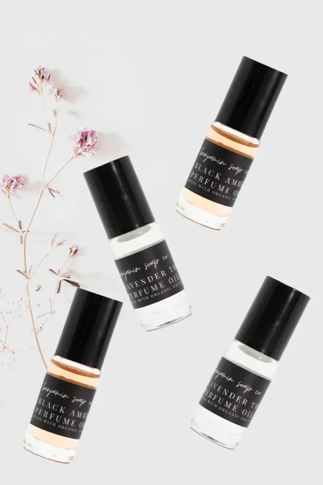 Three small bottles of Mini Perfume Oil with black caps, positioned on a white background with some dried flowers in the foreground.