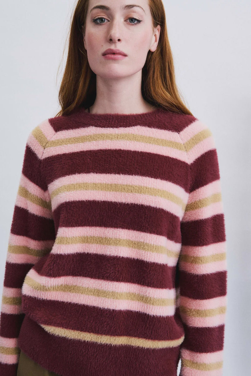 A woman wearing a fuzzy knit sweater with horizontal stripes in burgundy, light pink, and muted olive green, photographed against a plain light background.