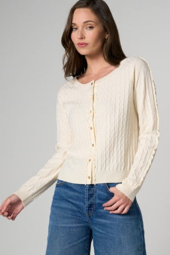 Woman wearing a cream blouse and blue jeans against a neutral background
