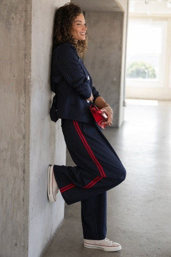 Woman in a navy tracksuit with red stripes leaning against a wall.