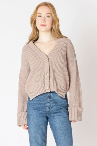 Woman wearing a beige cardigan and blue jeans on a white background