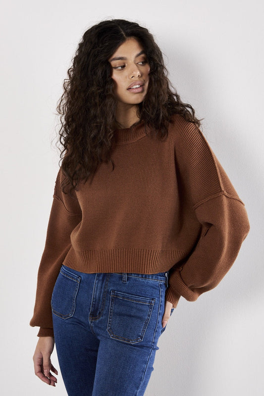 Woman wearing a brown sweater and blue jeans against a white background