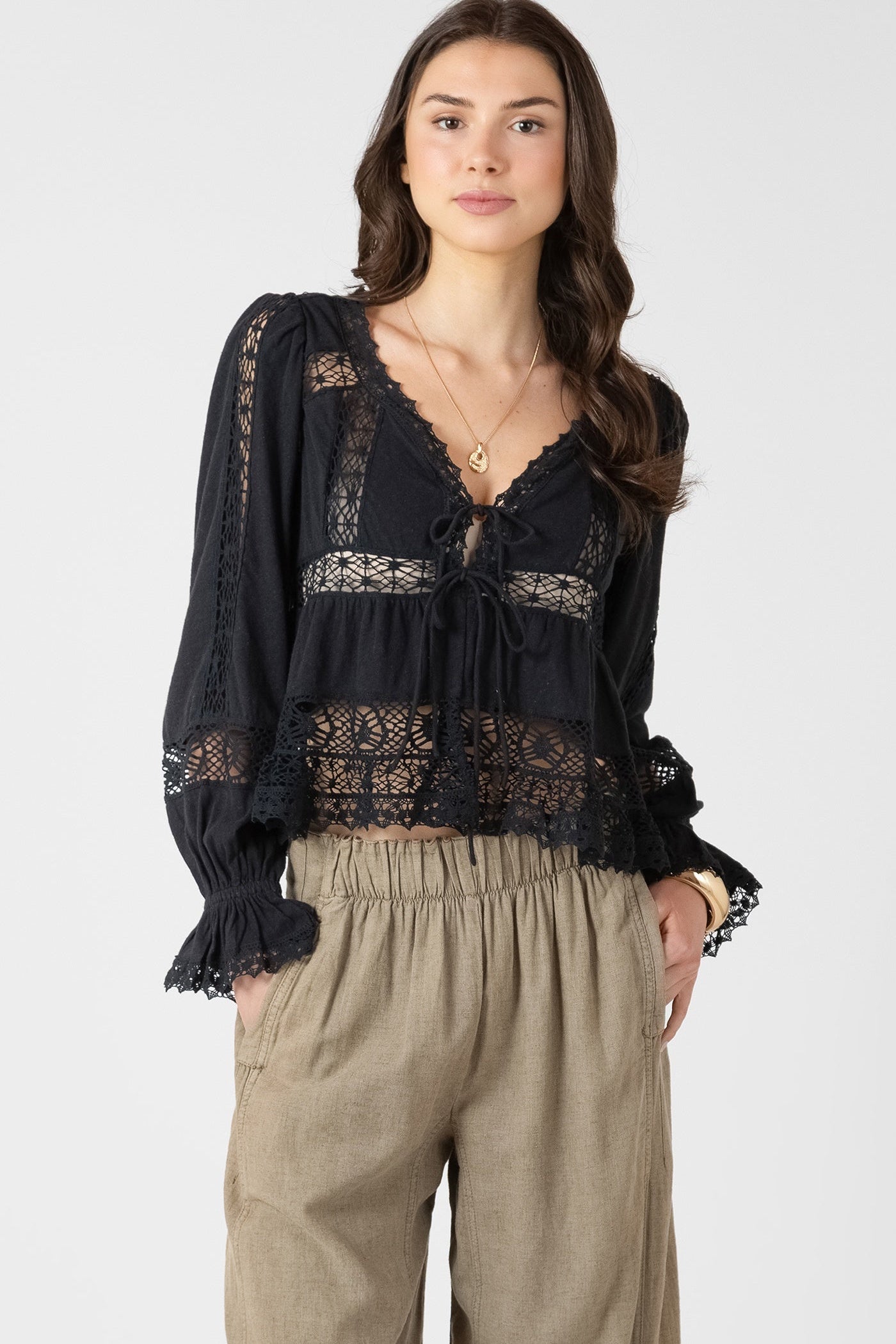 Woman wearing a black lace blouse and beige pants on a white background