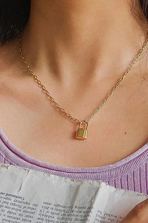 Gold lock necklace worn by a person with a purple top, sitting on a textured surface.