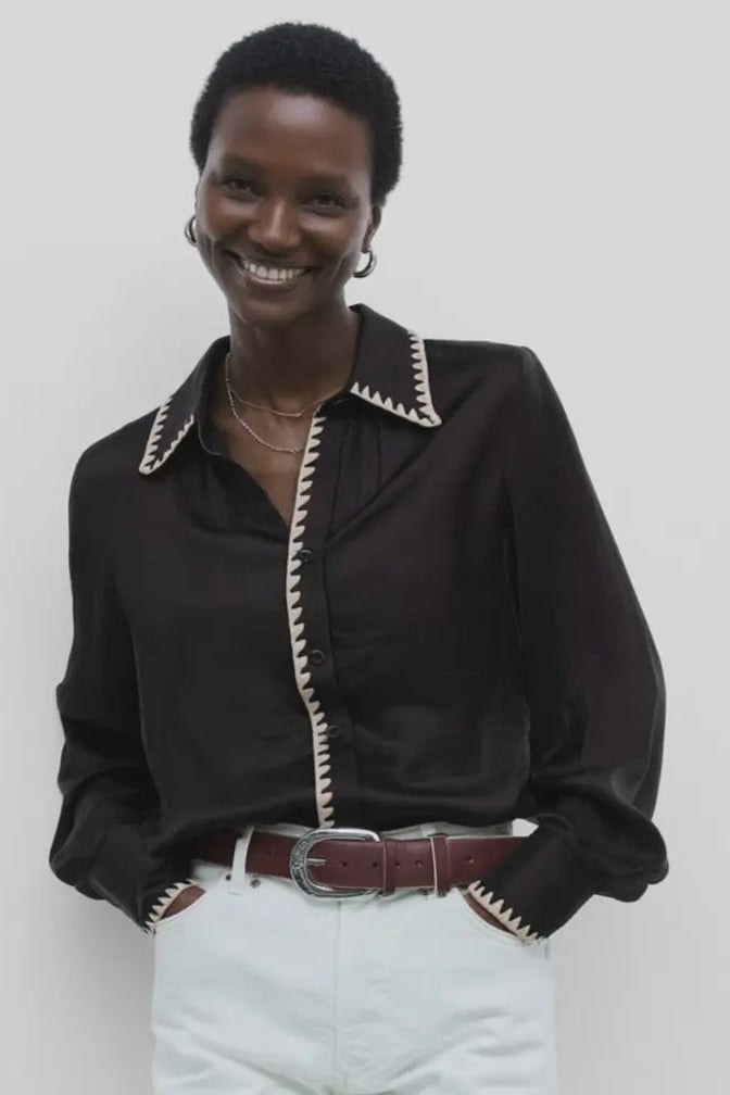 Person wearing a black blouse with white trim and light blue jeans against a plain background