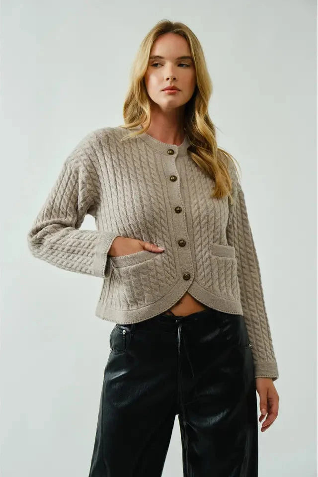 Woman wearing a beige knitted cardigan and black pants on a plain background