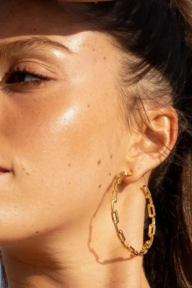 Close-up of a woman wearing gold hoop earrings with a clear blue sky background