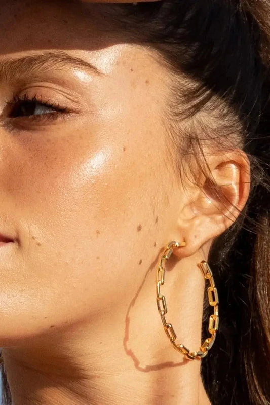 Close-up of a woman wearing gold hoop earrings with a clear blue sky background