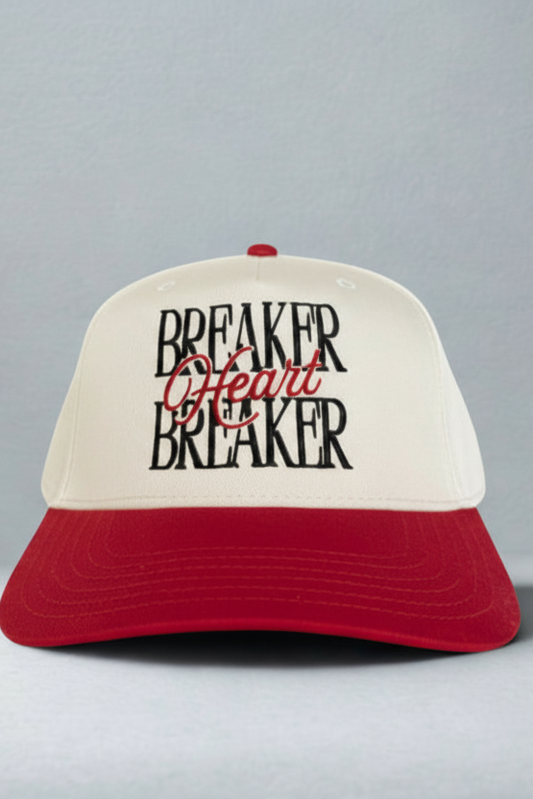 A two-tone trucker-style cap with an off-white front panel and a red brim. The front panel features the text 'BREAKER Heart BREAKER' in black and red embroidery, with a small red button on top.