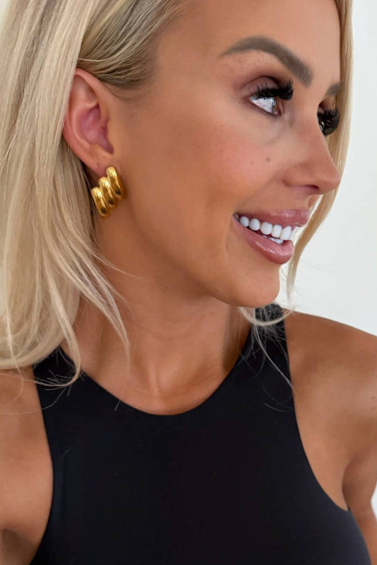 Woman wearing gold hoop earrings with a neutral background