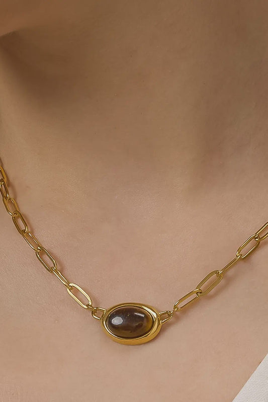 Gold necklace with a brown gemstone on a person wearing a beige top.