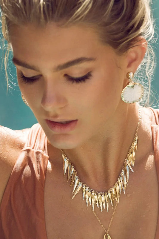 Woman wearing a gold necklace and earrings with a blurred blue background
