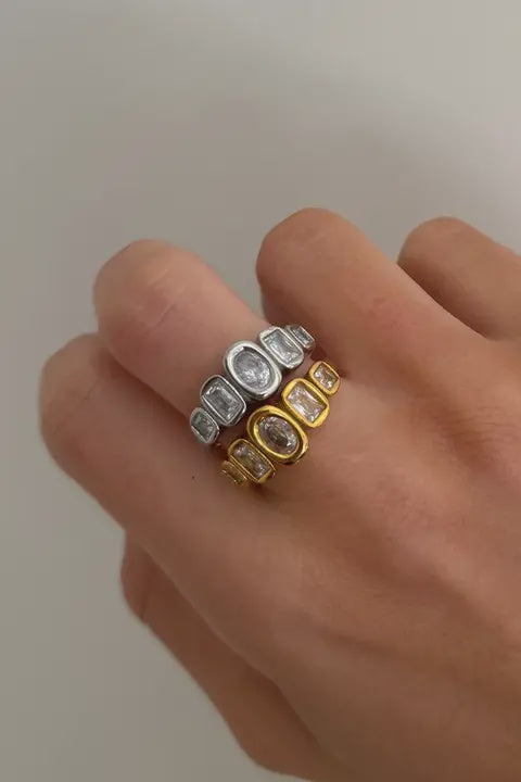 Hand wearing two diamond-studded rings on a plain background