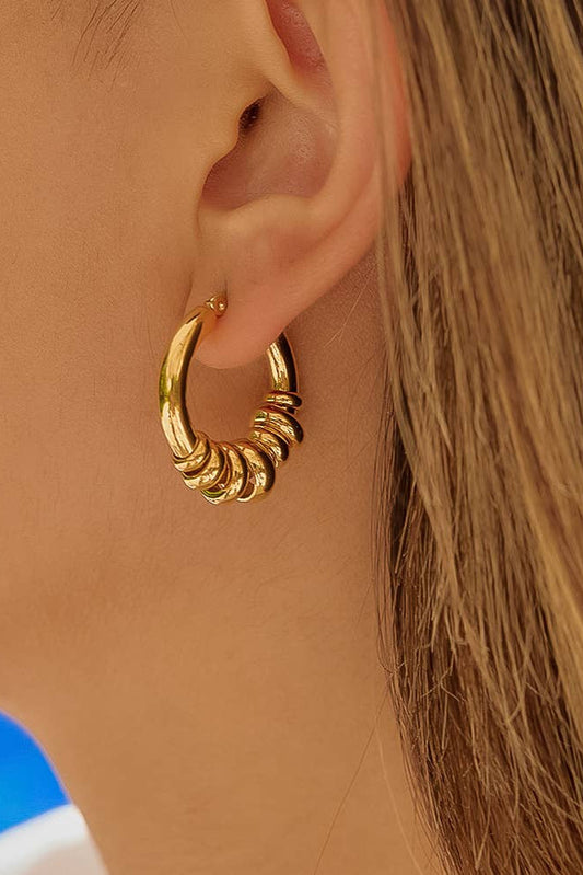 A close-up of a person's ear wearing a gold hoop earring with a twisted, layered spiral design.