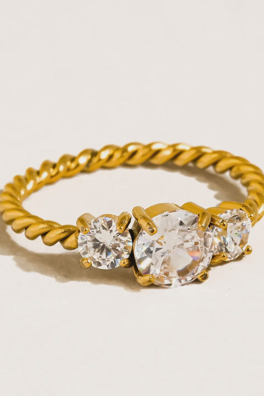 Gold ring with three clear gemstones on a light background