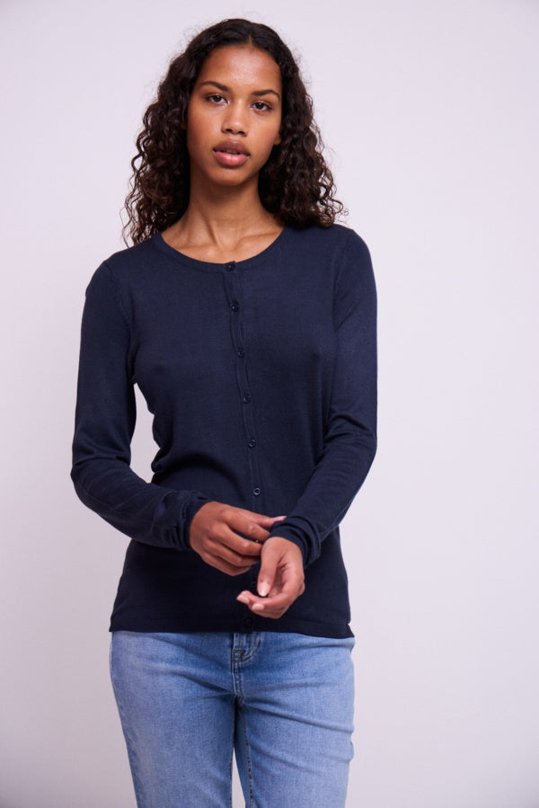 Woman wearing a navy long-sleeve shirt and light blue jeans against a white background