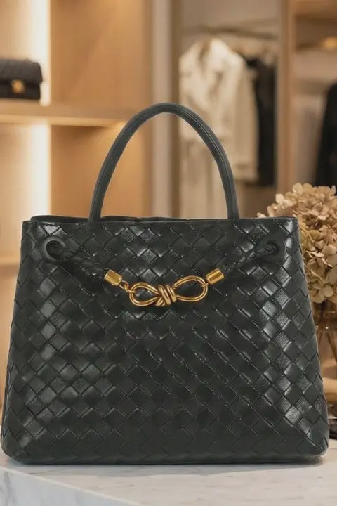 Black woven handbag with gold accents on a surface with a blurred background of shelves and clothing.