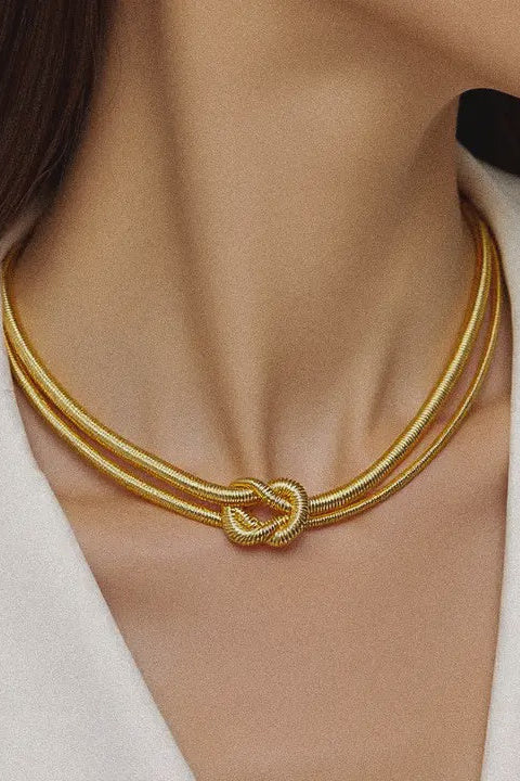 Gold necklace with a knot design worn by a person in a white blazer.