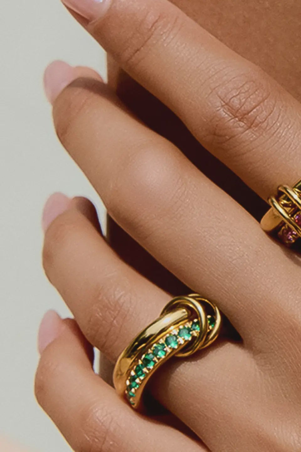 Close-up of a hand wearing two gold rings with gemstones on a neutral background